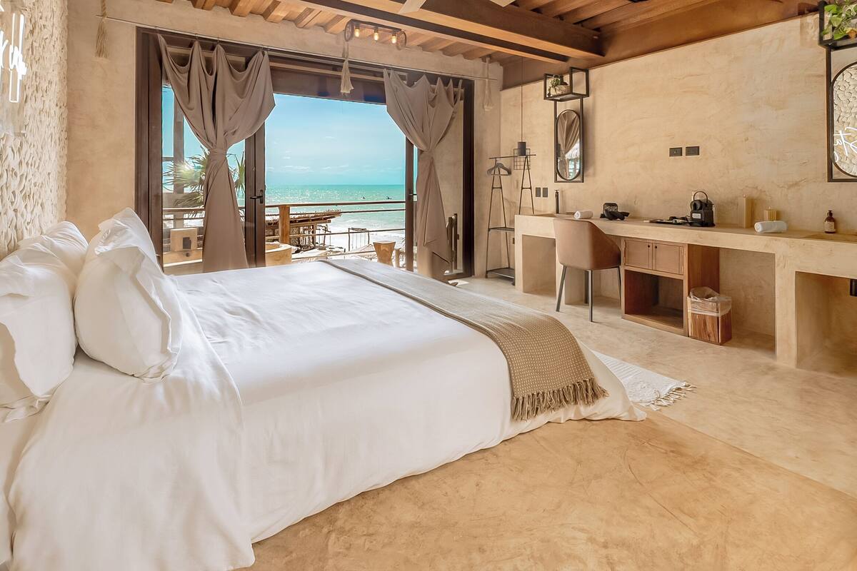 A bedroom with a large bed, a desk, and a view of the sea.