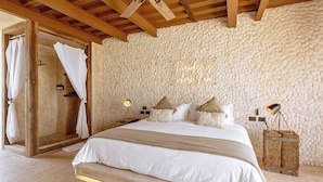 A bedroom with a large bed, a wooden ceiling, stone walls, a shower area, and a bedside lamp. - Awa Holbox Hotel Boutique - Beach Front (Isla Holbox)