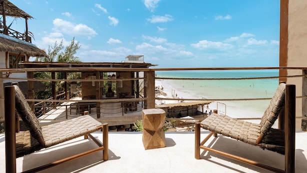 A beachside balcony with two wicker lounge chairs, a wooden table, and a thatched-roof structure. - Awa Holbox Hotel Boutique - Beach Front (Isla Holbox)