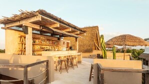 An outdoor bar area with a thatched roof, wooden stools, and a variety of bottles. - Awa Holbox Hotel Boutique - Beach Front (Isla Holbox)