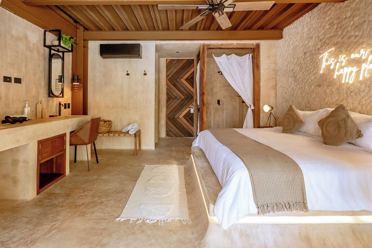 A bedroom with a bed, bedside table, chair, and a mirror.