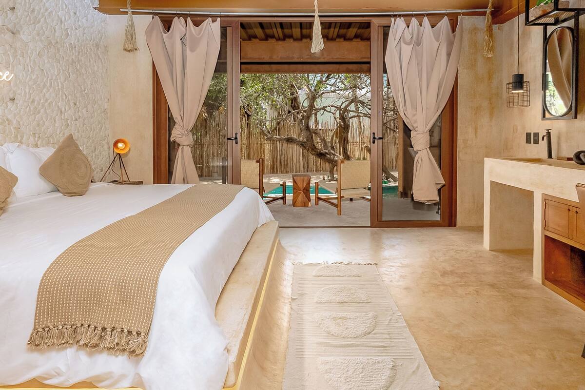 A bedroom with a bed, bedside lamp, and a view of an outdoor pool area.