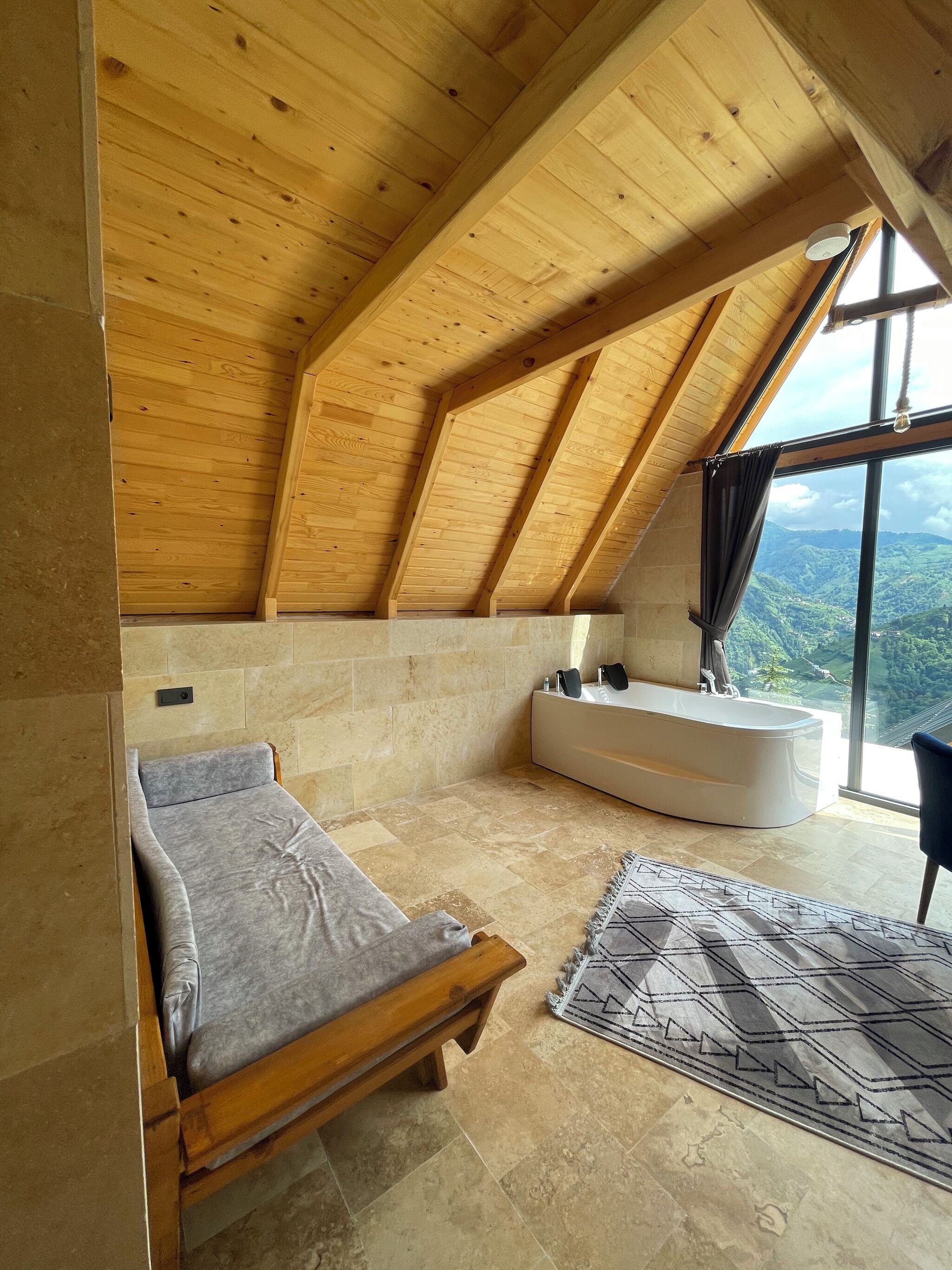 Ein Schlafzimmer mit schrägem Dach, einem Bett, einer Badewanne und Blick auf eine Berglandschaft.