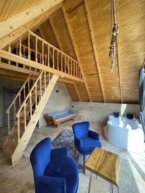 A spacious loft with a wooden staircase, a stone wall, a blue sofa, a small table, and a bathtub. - Toli Bungalow Tatil Koyu (Pazar)