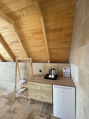A compact room with a wooden ceiling, a small white refrigerator, a wooden shelf with a kettle, and a towel rack. - Toli Bungalow Tatil Koyu (Pazar)
