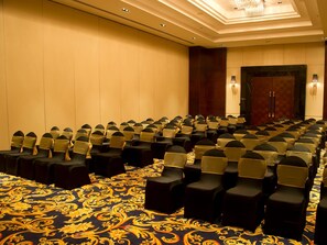 A conference room with rows of chairs, a patterned carpet, and a chandelier.