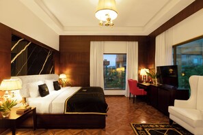 A hotel room with a bed, a desk with a chair, a TV, and a large window with curtains.