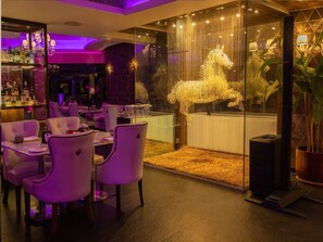 A bar area with a glass partition, a decorative horse sculpture, and a seating area with cushioned chairs and tables.