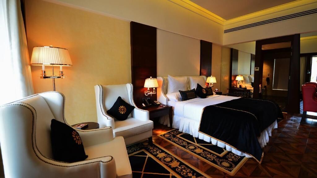 A hotel room with a bed, two bedside tables with lamps, a chair, a desk, and a patterned rug.