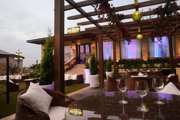 An outdoor dining area with wicker furniture, white cushions, and empty wine glasses on a table.