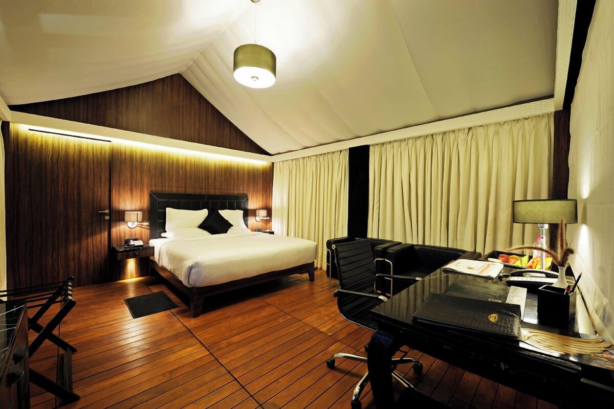 A hotel room with a bed, desk, chair, lamp, and curtains.