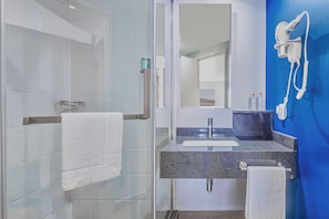 A modern bathroom with a glass shower, a sink with a granite countertop, and a hairdryer mounted on the wall. - One Mazatlán (Mazatlan)