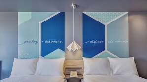 A modern hotel room with a bed, a bedside table with a phone, and geometric wall art with text. - One Mazatlán (Mazatlan)