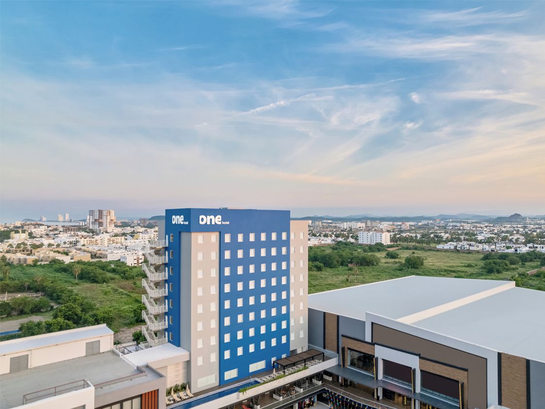 Un hotel de diseño moderno, con una fachada azul y blanca destacada y vistas a un paisaje urbano de fondo.