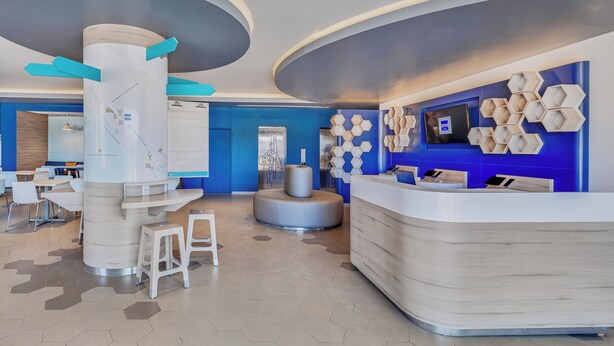 A modern reception area with a curved desk, seating, and a wall-mounted TV. - One Mazatlán (Mazatlan)