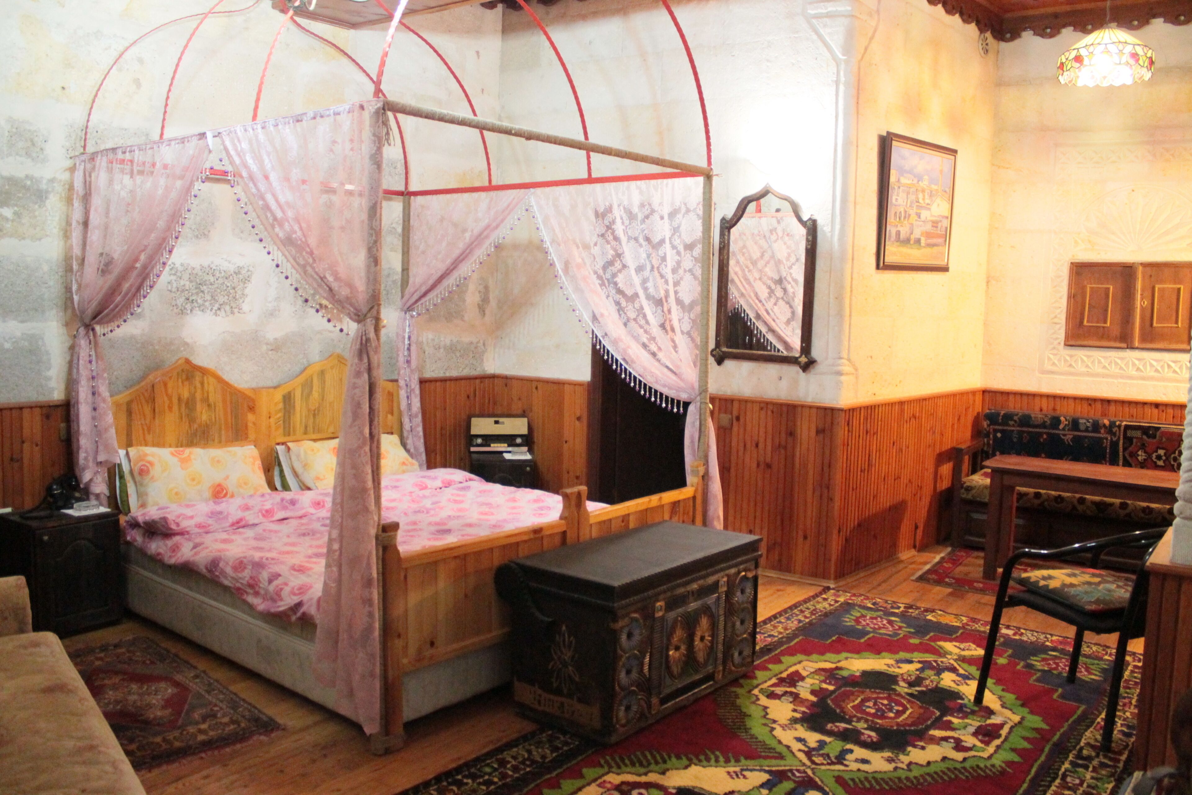 A room with a four-poster bed, a wooden bench, a small table, and a patterned rug.