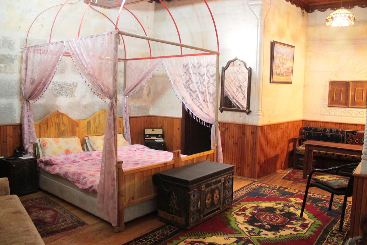 A room with a four-poster bed, a wooden bench, a small table, and a patterned rug.