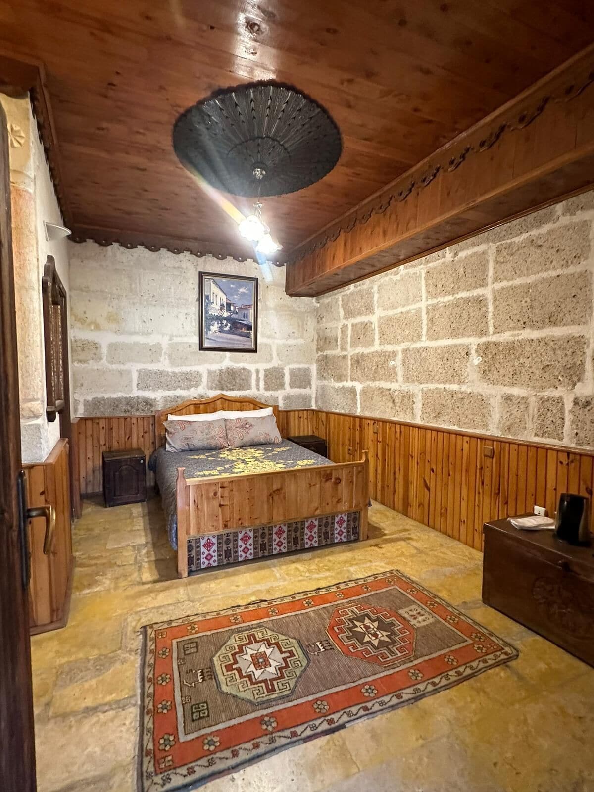 A room with a wooden bed, a stone wall, a wooden ceiling, and a patterned rug.