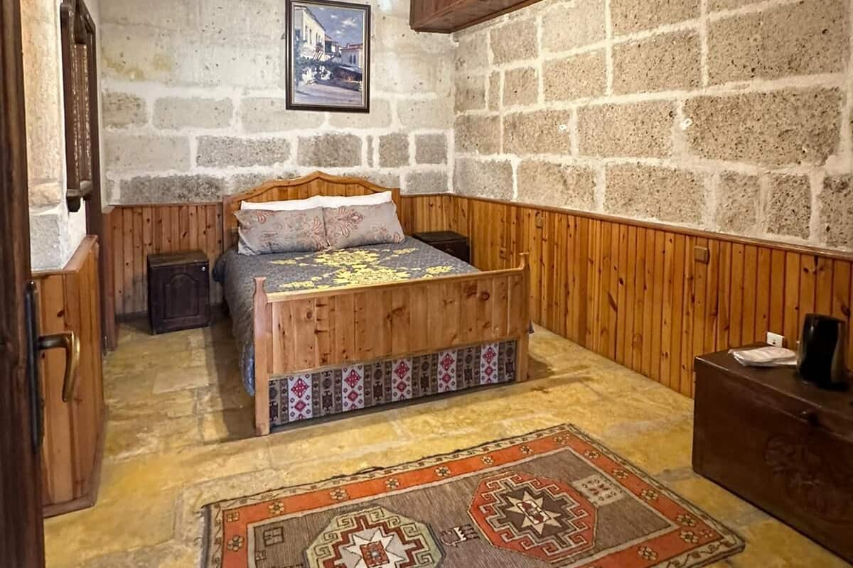 A room with a wooden bed, a stone wall, a wooden ceiling, and a patterned rug.