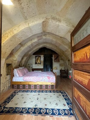 Ein Schlafzimmer mit Steindecke, einem Bett mit gemusterten Textilien, einem Holzkleiderschrank und einem Teppich.