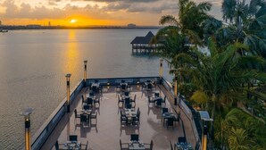 A waterfront restaurant with outdoor seating, a view of the sunset, and a distant overwater structure. - Delta Hotels Marriott, Dar es Salaam (Dar es Salaam)