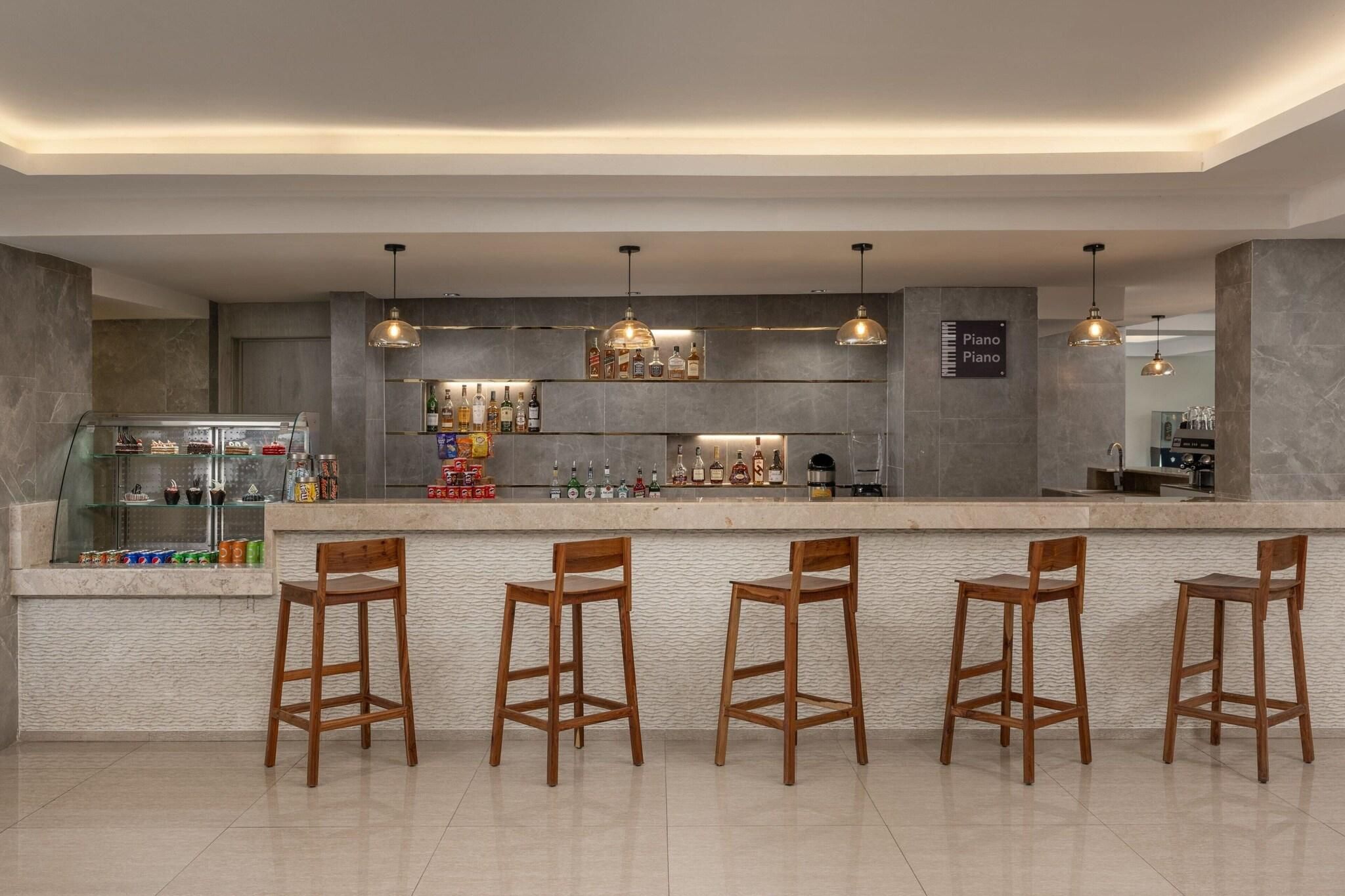 A bar area with a marble countertop, wooden stools, hanging pendant lights, and a variety of bottles and snacks.