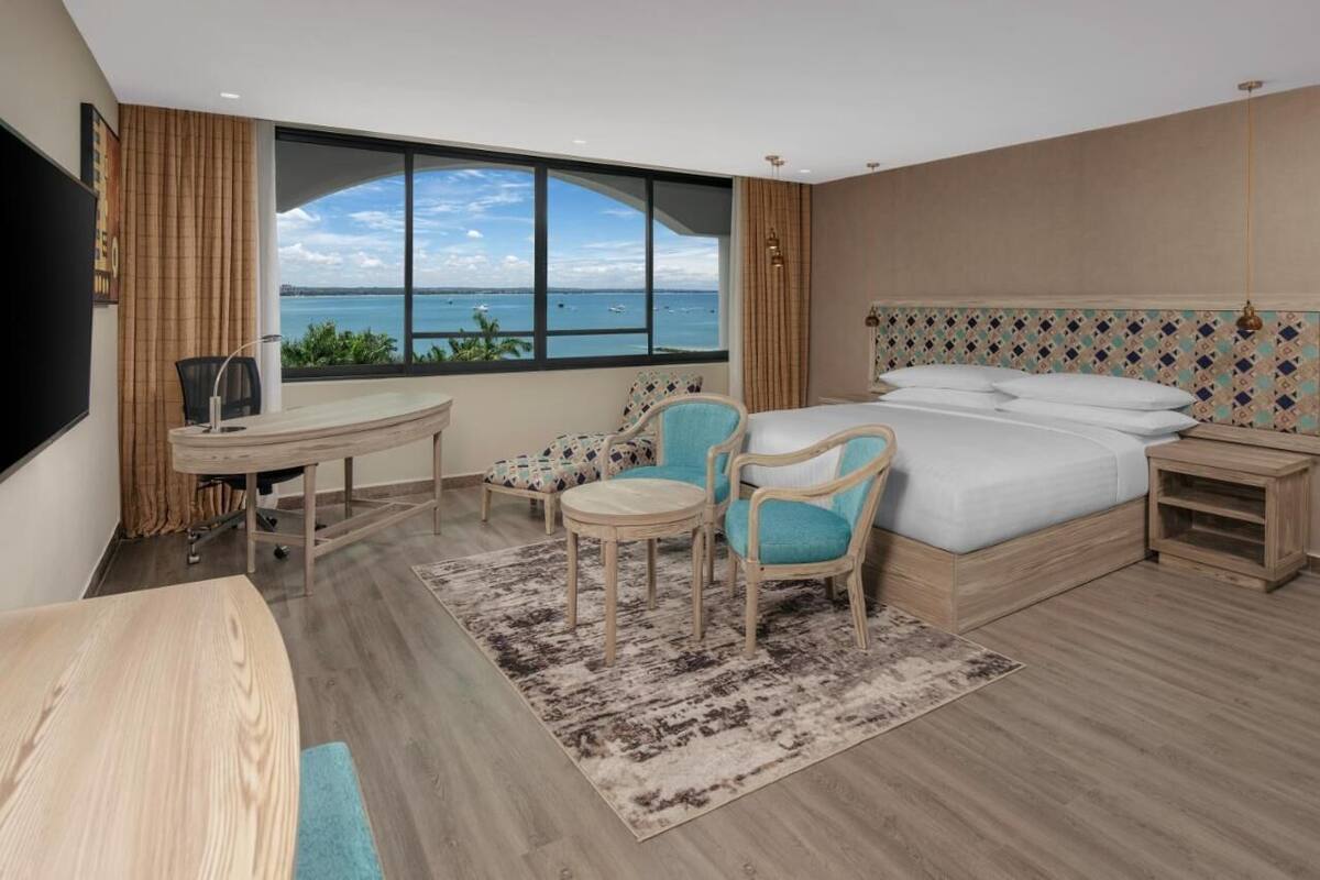 Habitación de hotel con una ventana grande, una cama, un escritorio y dos sillas.