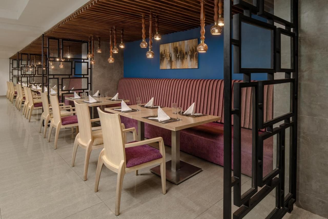 A restaurant with wooden tables and chairs, a red cushioned bench, and pendant lighting.