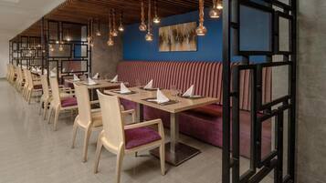 Un restaurante con mesas y sillas de madera, un banco con cojín rojo e iluminación colgante.