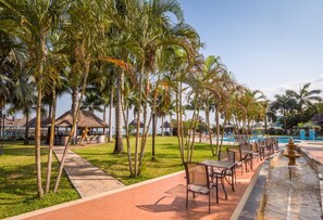 A resort with a pool, palm trees, outdoor seating, and a thatched-roof structure. - Delta Hotels Marriott, Dar es Salaam (Dar es Salaam)