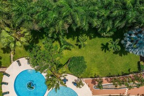 Vue aérienne d’un complexe hôtelier doté d’une piscine circulaire, de palmiers et d’une pelouse bien entretenue.