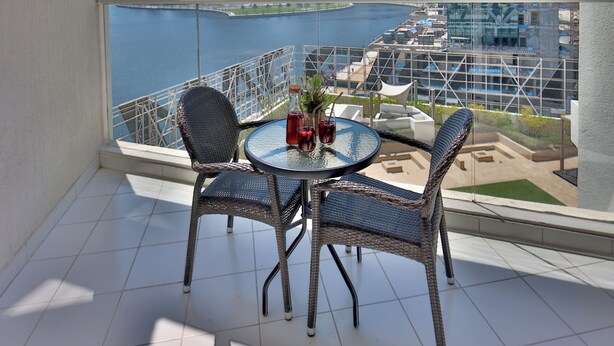A balcony with a table and chairs, a view of a city skyline, and a body of water.