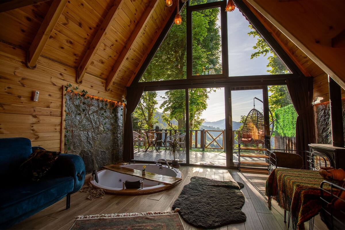 A cozy room with a wooden ceiling, a large window, a blue sofa, a round table, and a fireplace.