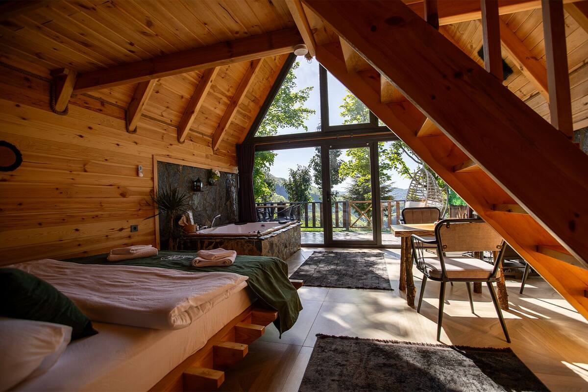 A wooden cabin with a loft bedroom, a bathroom with a bathtub, and a dining area with a view.