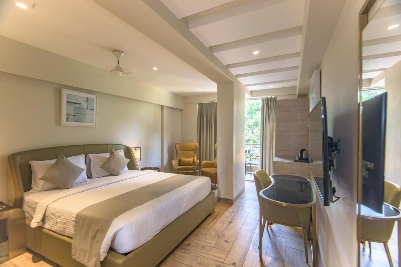 A hotel room with a large bed, a desk, a chair, a TV, and a balcony.