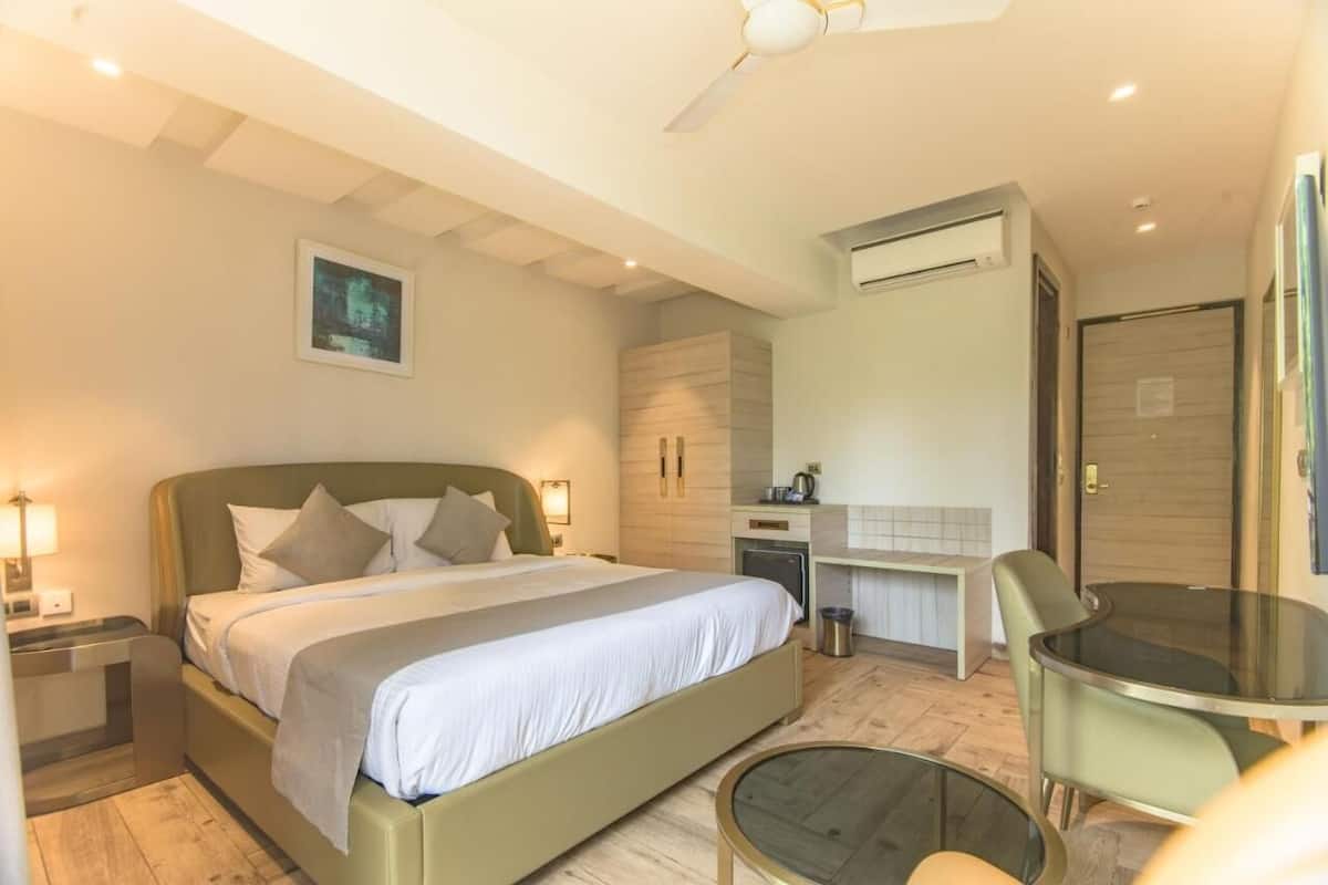 A modern hotel room with a bed, bedside table, desk, chair, and a small round table.