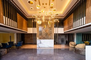 A spacious lobby with a marble reception desk, modern seating, and a unique ceiling light fixture. - The Fern Residency, Calangute (Calangute)