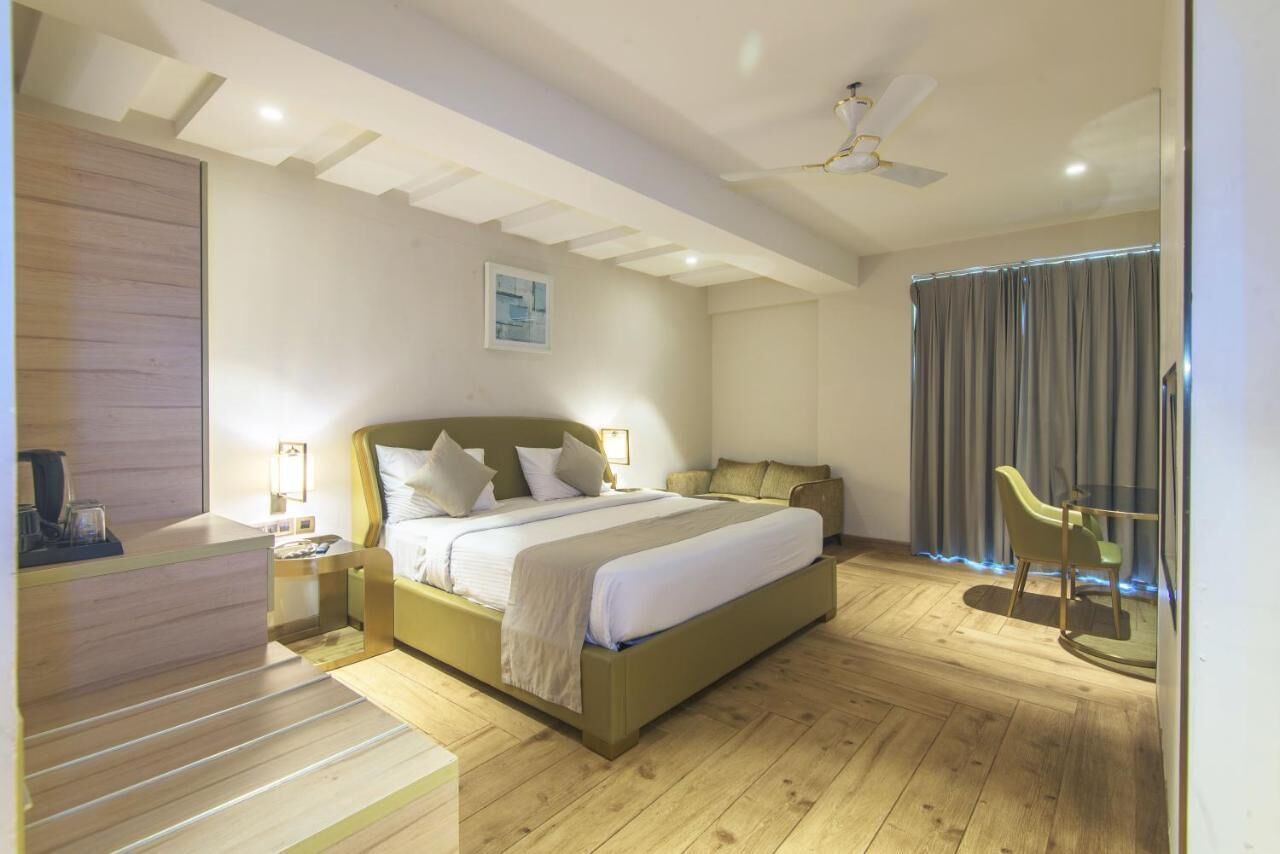 A hotel room with a bed, bedside tables, a desk, a chair, a ceiling fan, and a window with curtains.