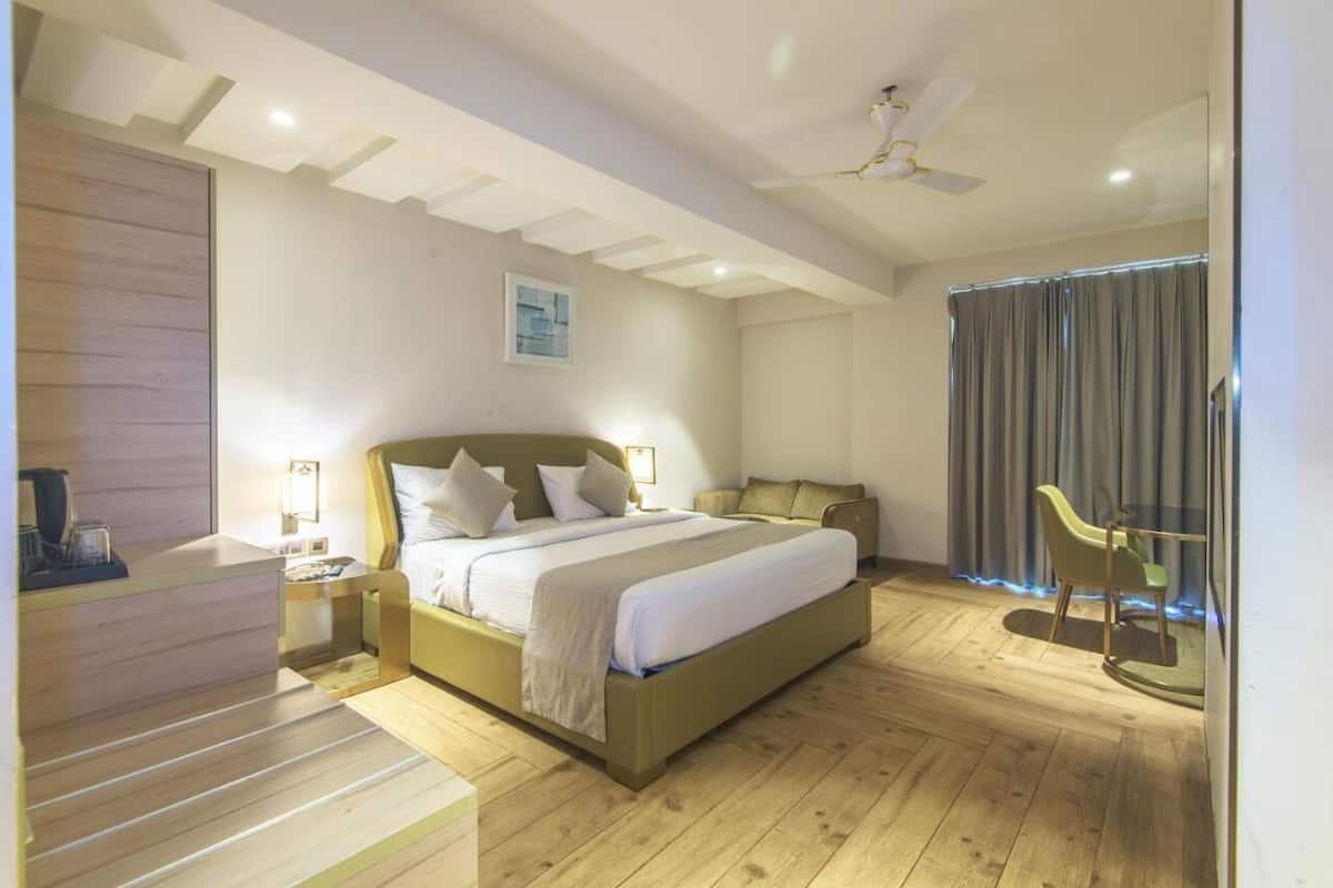 A hotel room with a bed, bedside tables, a desk, a chair, a ceiling fan, and a window with curtains.