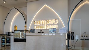 Una barra de café con un letrero de neón que dice 'Campero Lounge & Cafe', una vitrina de vidrio y una máquina de café.