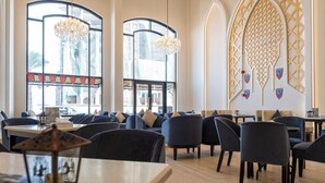 Un restaurante con techos altos, ventanas amplias y candelabros. Mesas y sillas dispuestas para comer.