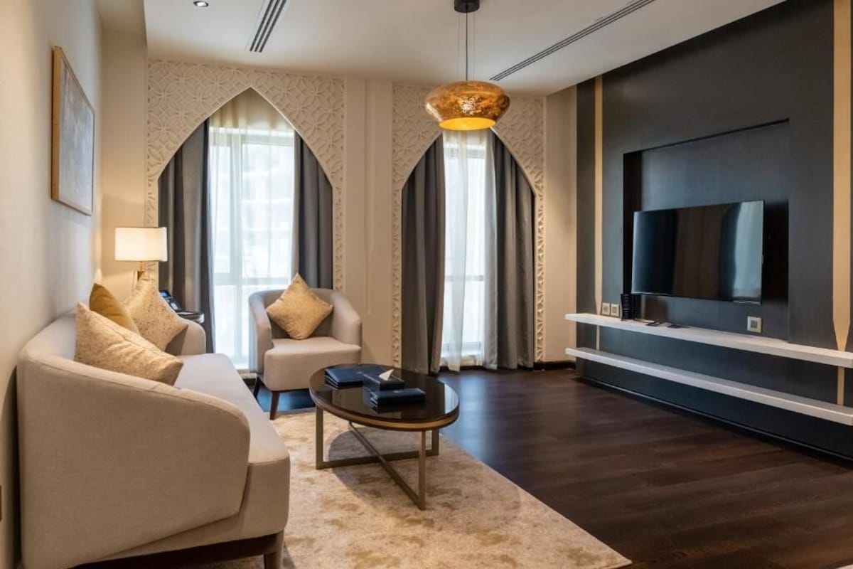 Ein modernes Wohnzimmer mit Sofa, Sesseln, Couchtisch und einem flachbildfernseher an der Wand.