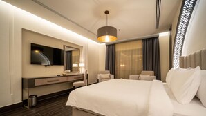 Habitación de hotel con una cama grande, un escritorio con espejo, televisor y una lámpara colgante moderna.
