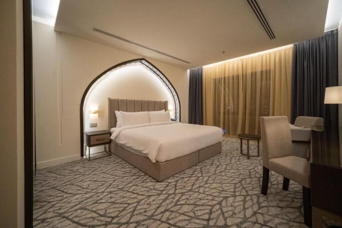 Ein Hotelzimmer mit einem großen Bett, einem kleinen Tisch, einem Sessel und einem Spiegel.