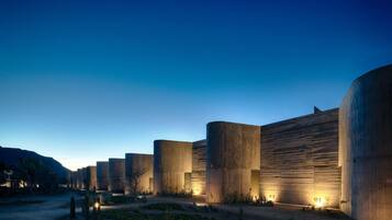 A series of cylindrical concrete structures with illuminated entryways, set in a desert-like environment with sparse vegetation.