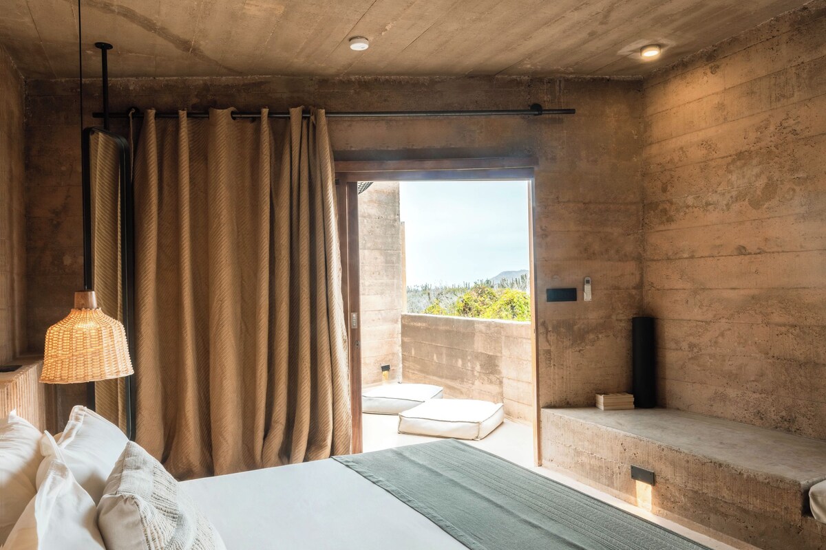 Een slaapkamer met een groot bed, uitzicht naar buiten en een betonnen plafond.