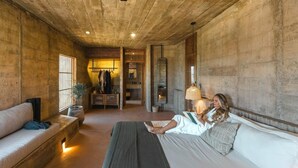 Una habitación con una cama, un banco, una lámpara colgante y un espejo en la pared.