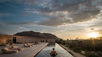 Un hombre en una piscina con un paisaje desértico y montañas al fondo.