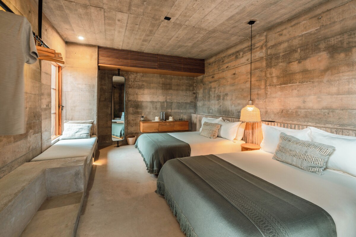 Un dormitorio moderno con dos camas, un banco de madera, una mesita y una ventana.