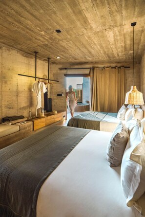 Une chambre avec un grand lit, une commode en bois, un luminaire suspendu et une vue sur l’extérieur.